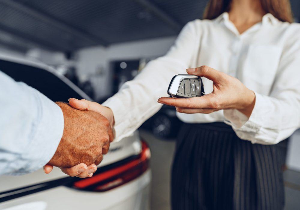 Car seller and buyer handshake at car dealership against a new car background